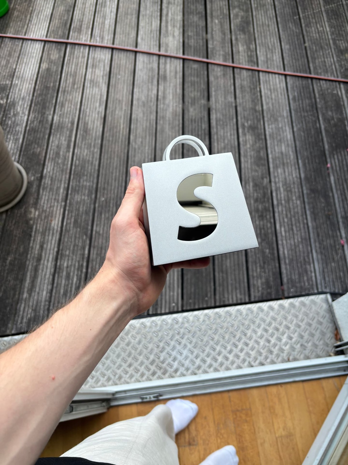 Silver Shopify "S" shopping bag award held in a hand